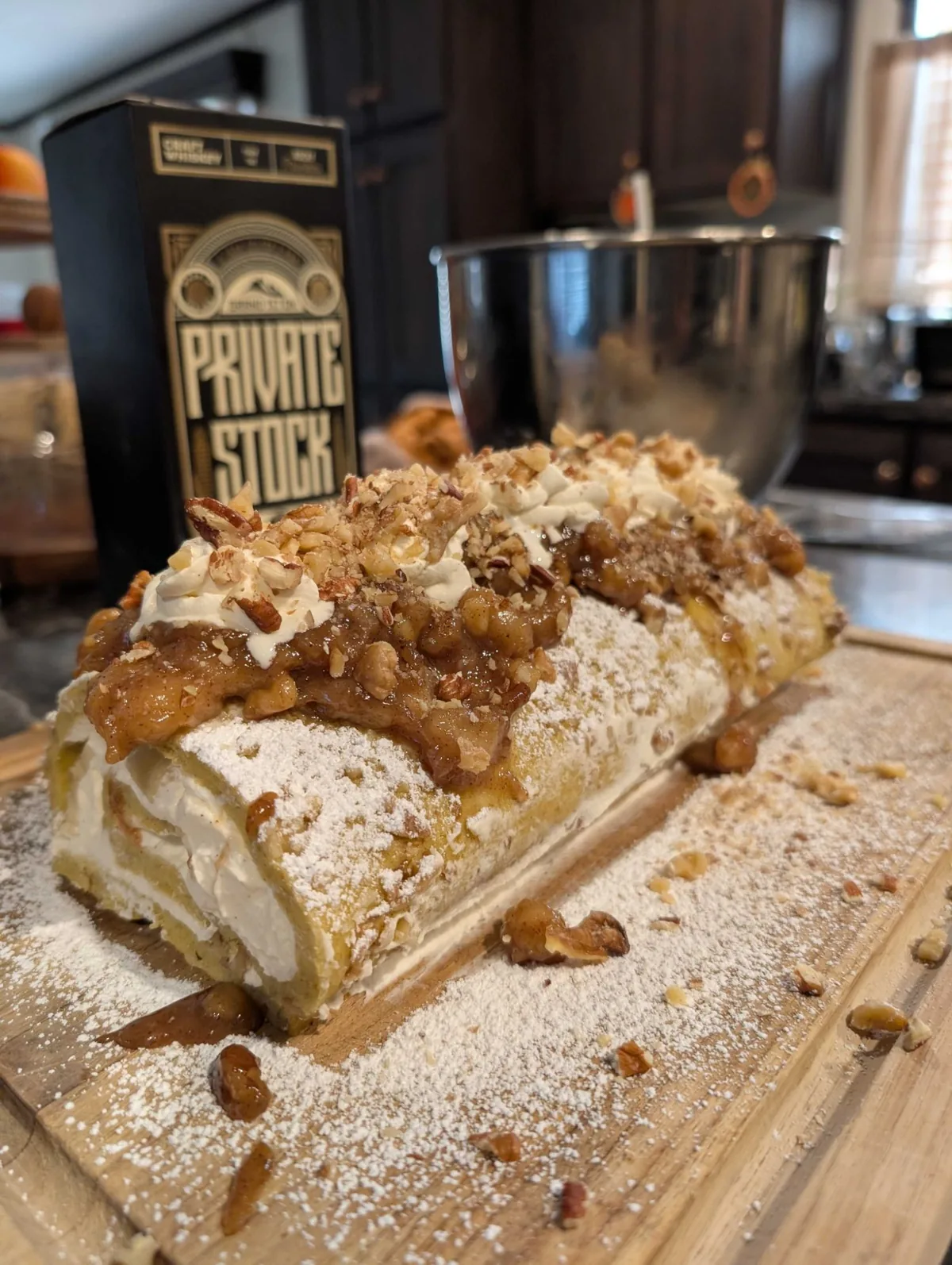 The bananas foster roll head-on, caramel dripping onto the board between scattered pecans