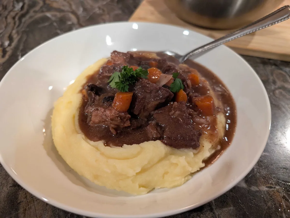 Beef bourguignon with carrots and glossy red wine sauce in a well of creamy mashed potatoes, topped with parsley