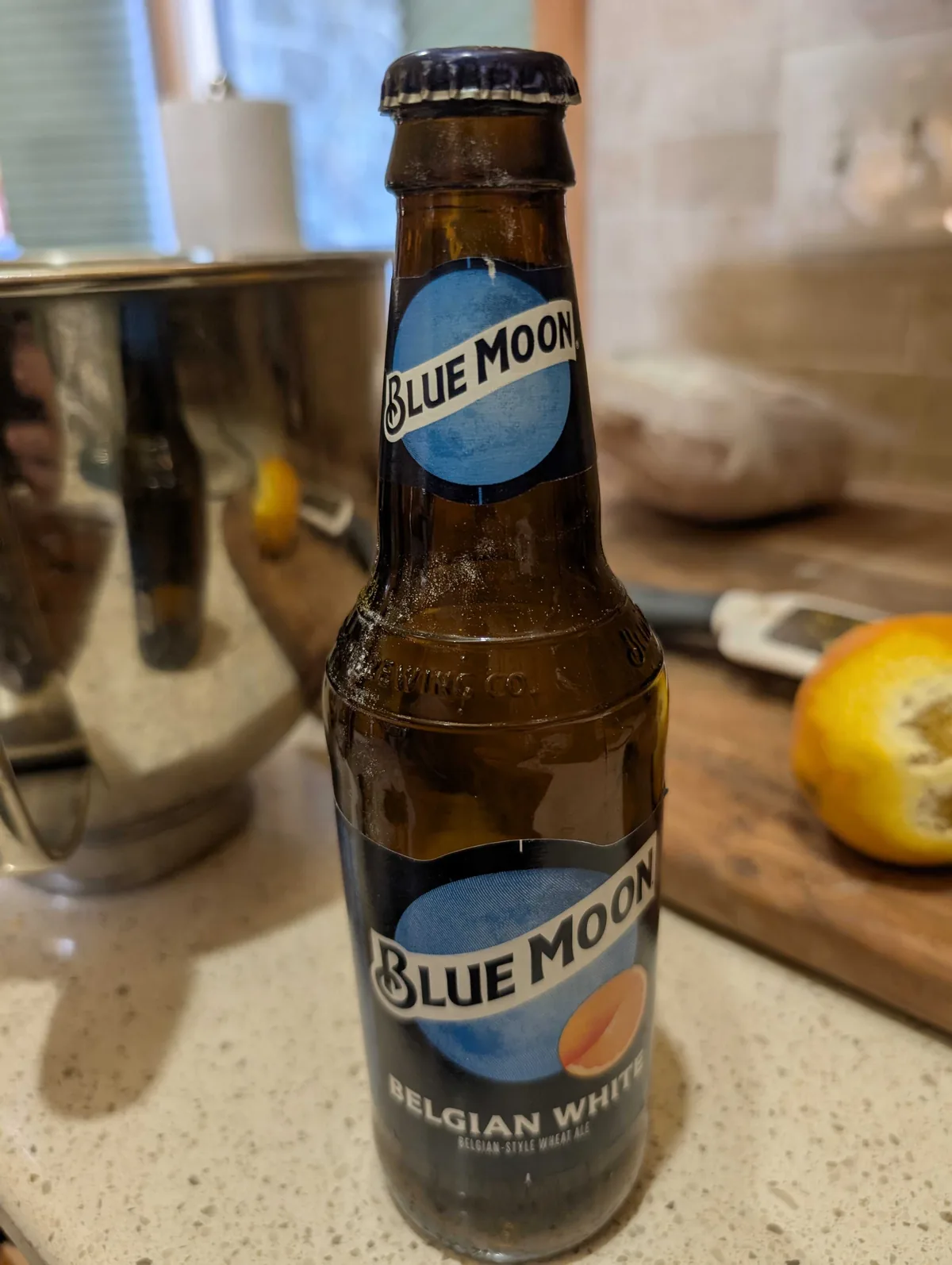 A bottle of Blue Moon Belgian White on the counter beside the mixing bowl and a zested orange