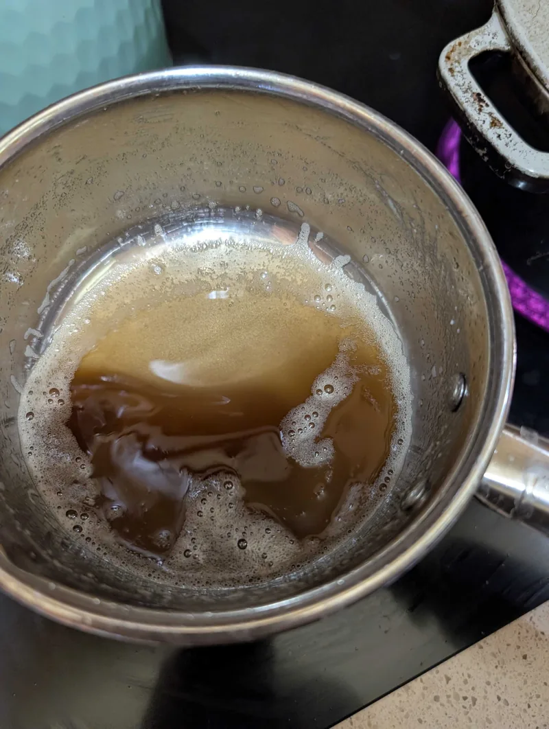 Salted butter browned to a deep amber in a small steel saucepan, still foaming at the edges