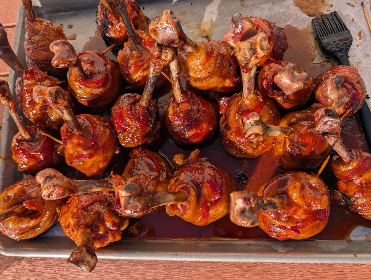 A tray packed with finished chicken lollipops, glazed deep mahogany red and standing upright on their bones