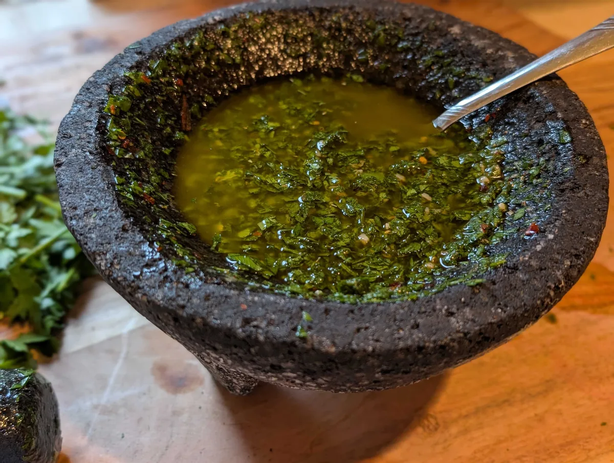 Looking into the molcajete at the glossy green chimichurri, flecked with chili