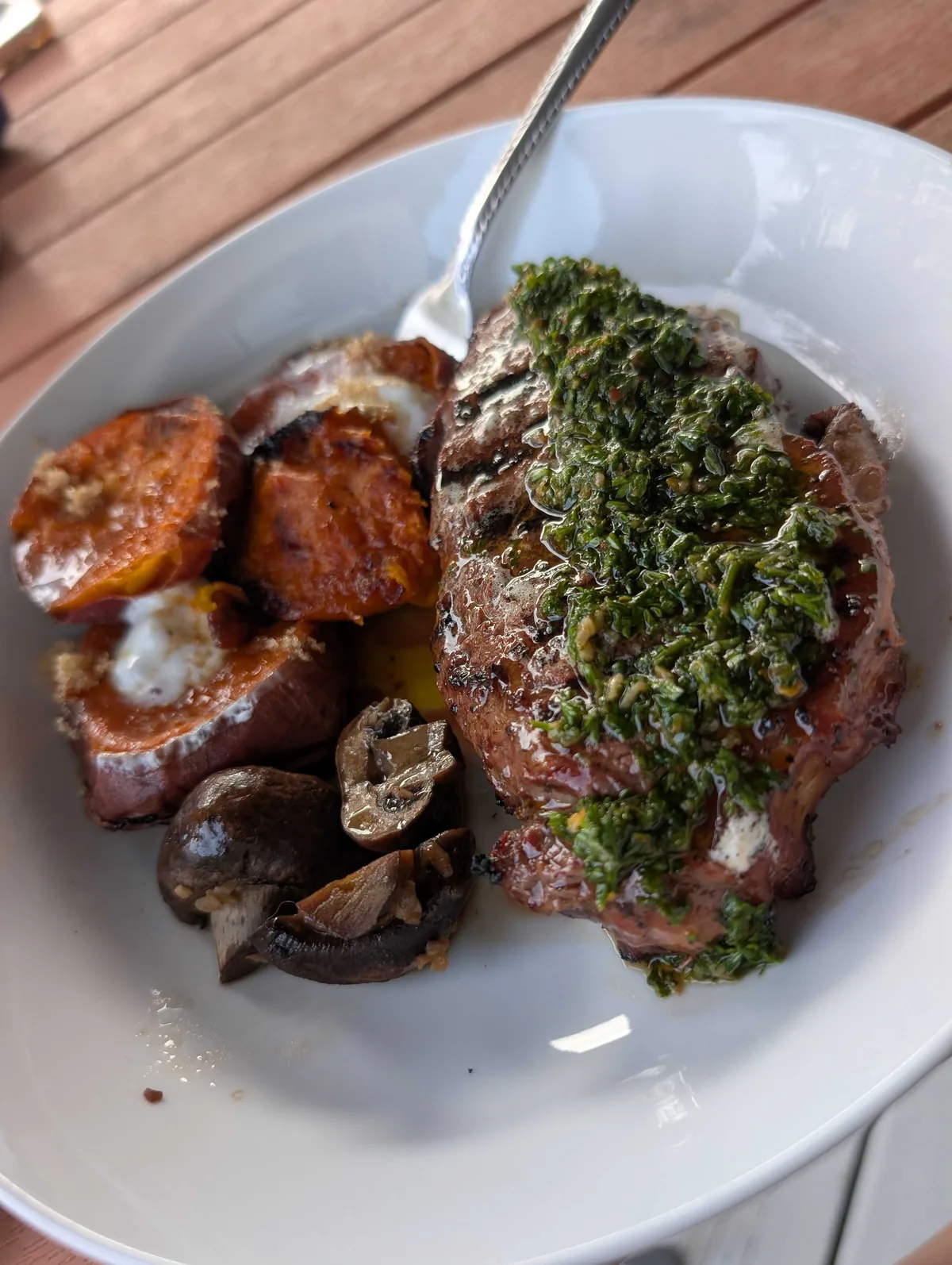 Chimichurri spooned over a sliced grilled steak, with sweet potatoes and mushrooms alongside