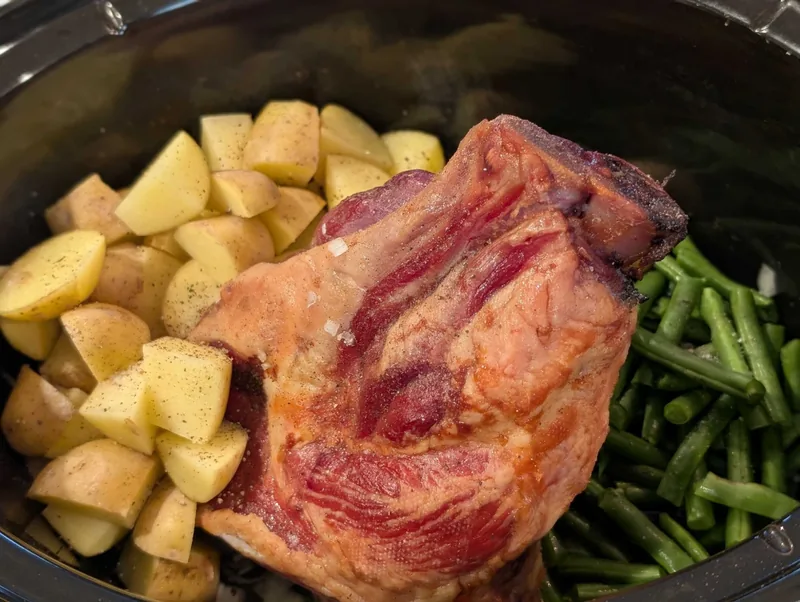 Little potatoes dusted with pepper and herbs packed beside a smoked ham hock and green beans in the crockpot