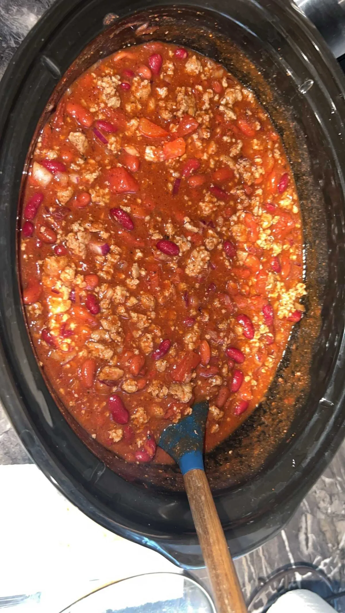 A pot of thick red venison chili with kidney beans and diced tomatoes, a wooden spatula resting in it