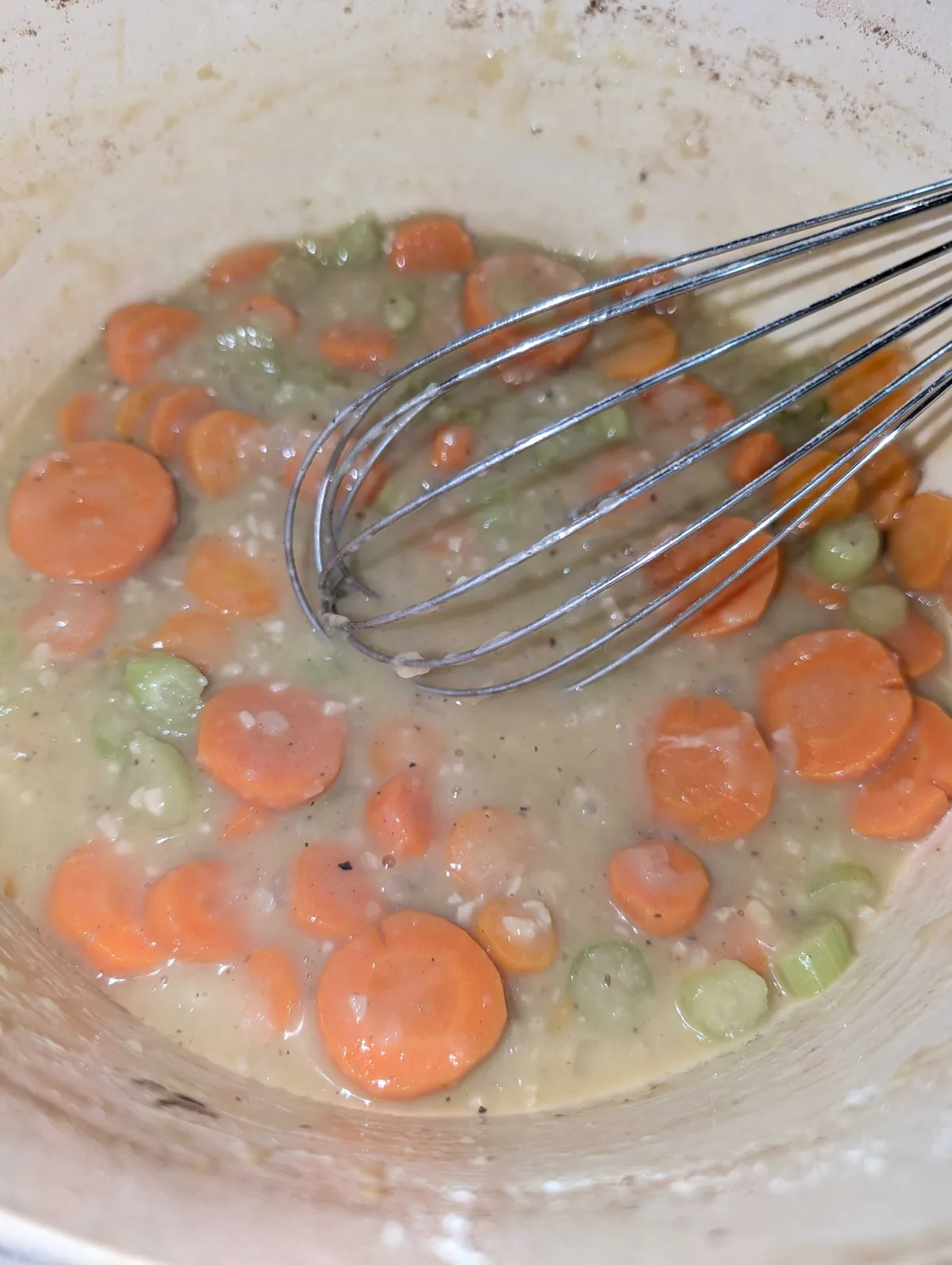 A whisk in the thickening gravy, studded with carrot and celery slices