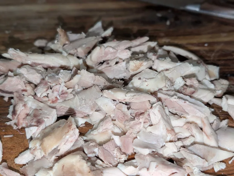 A pile of tender drumstick meat pulled from the bone on a dark wooden board