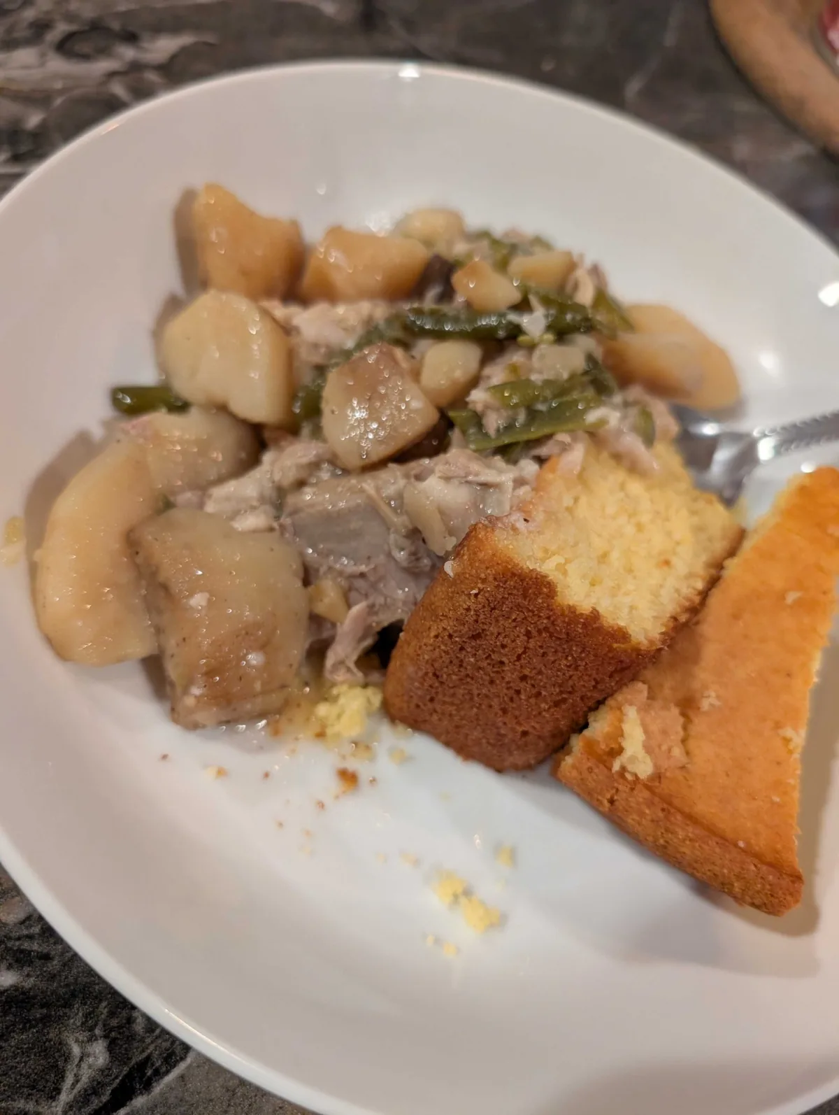 A bowl of shredded ham hock, green beans and potatoes with two wedges of honey cornbread