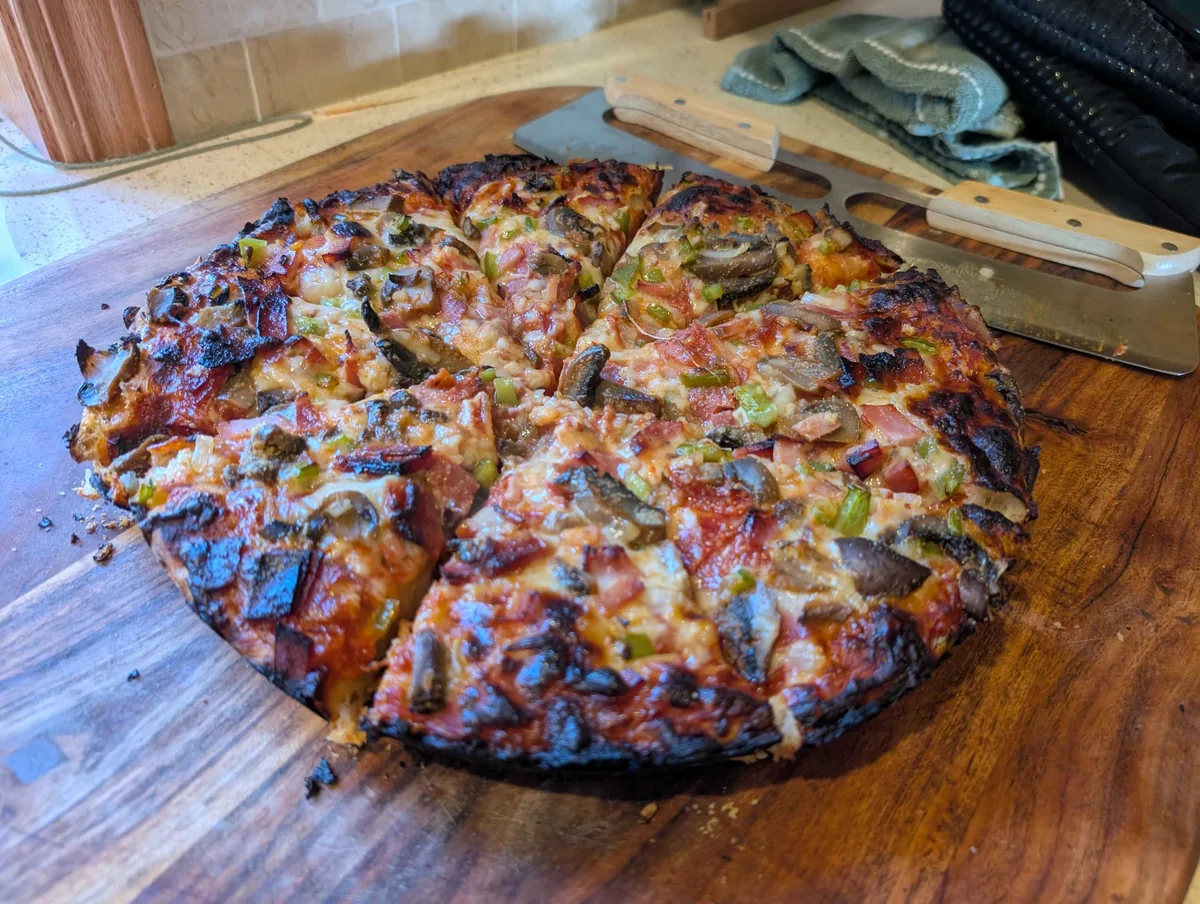 The whole pan pizza turned out onto a wooden board and cut into wedges