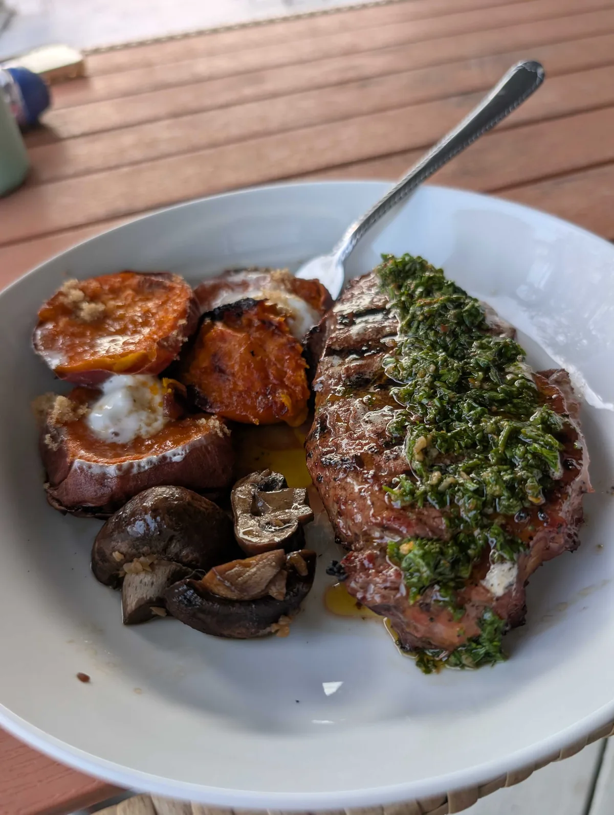 Close up of the grill-marked steak under a thick layer of chimichurri, sweet potatoes with brown sugar beside it