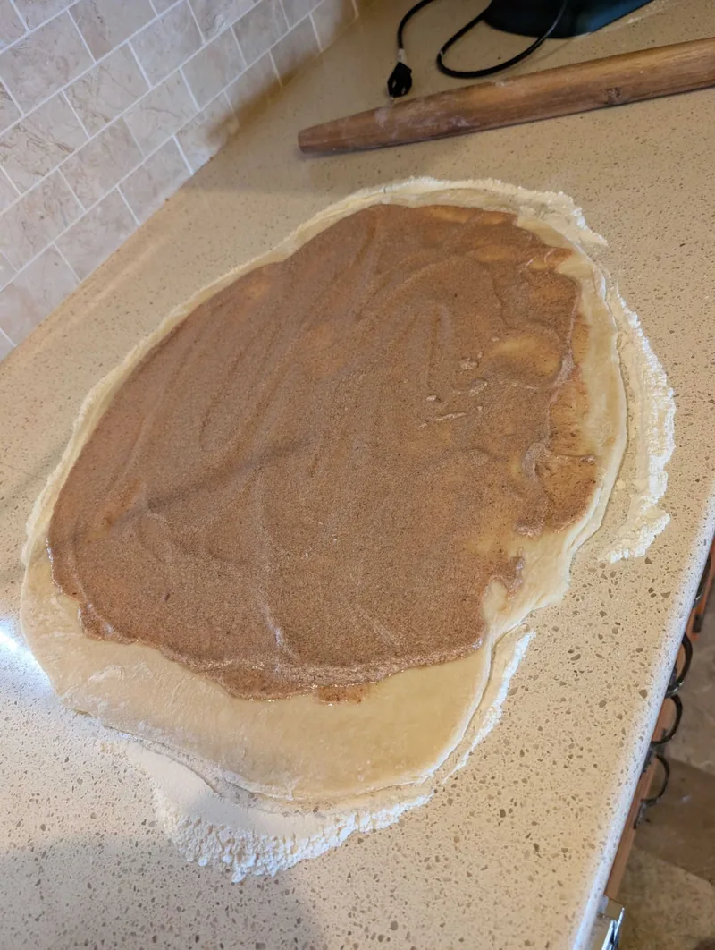 Rolled-out dough on a floured counter, spread edge to edge with butter, brown sugar and cinnamon