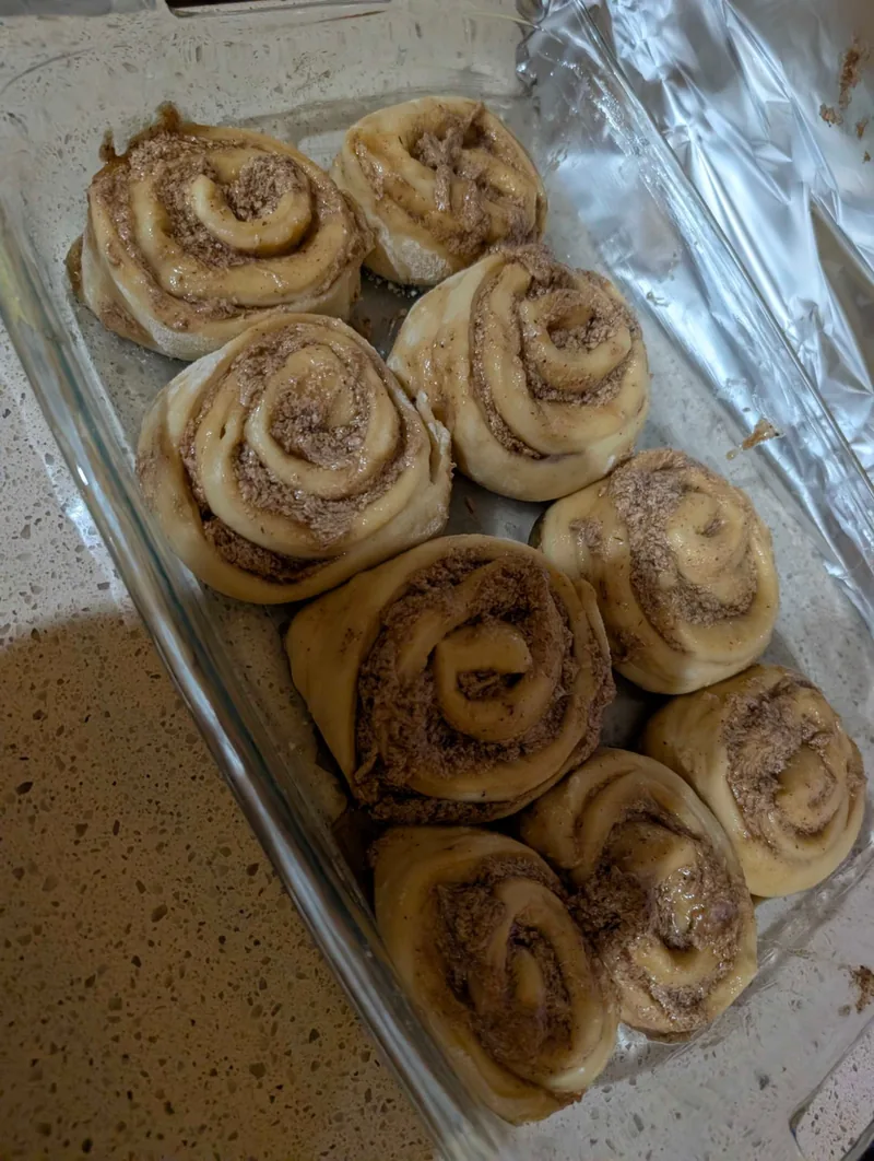 Sliced, unbaked cinnamon rolls arranged in a glass baking dish, ready for the second rise