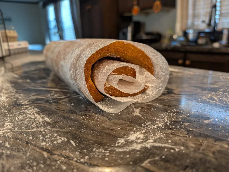 The hot sponge rolled up inside a sugar-dusted towel on a marble counter, cooling in its curl