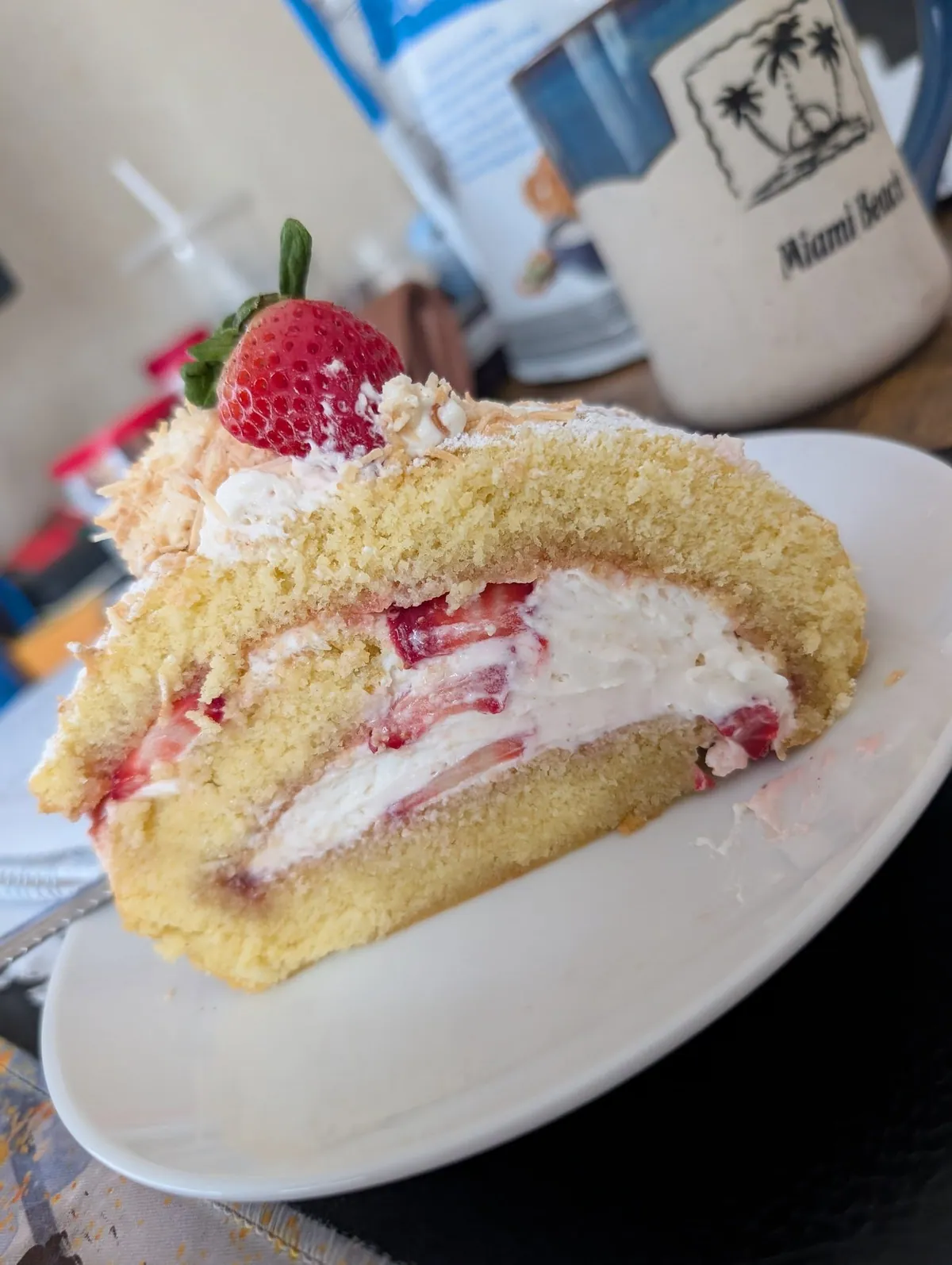 A cut slice of the roll on a white plate, showing the spiral of sponge, strawberry jam and whipped cream